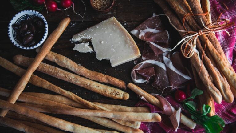 Grisini sa parmezanom, pršutom i maslinama na drvenoj dasci