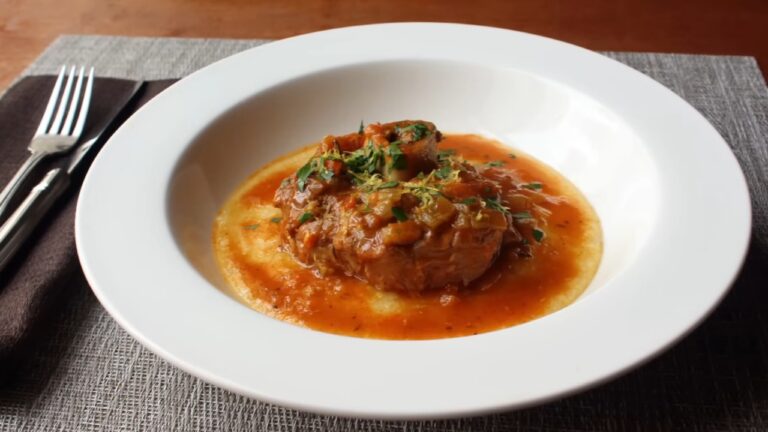Osso buco u bogatom paradajz sosu poslužen preko kremaste palente i posut svežim začinskim biljem